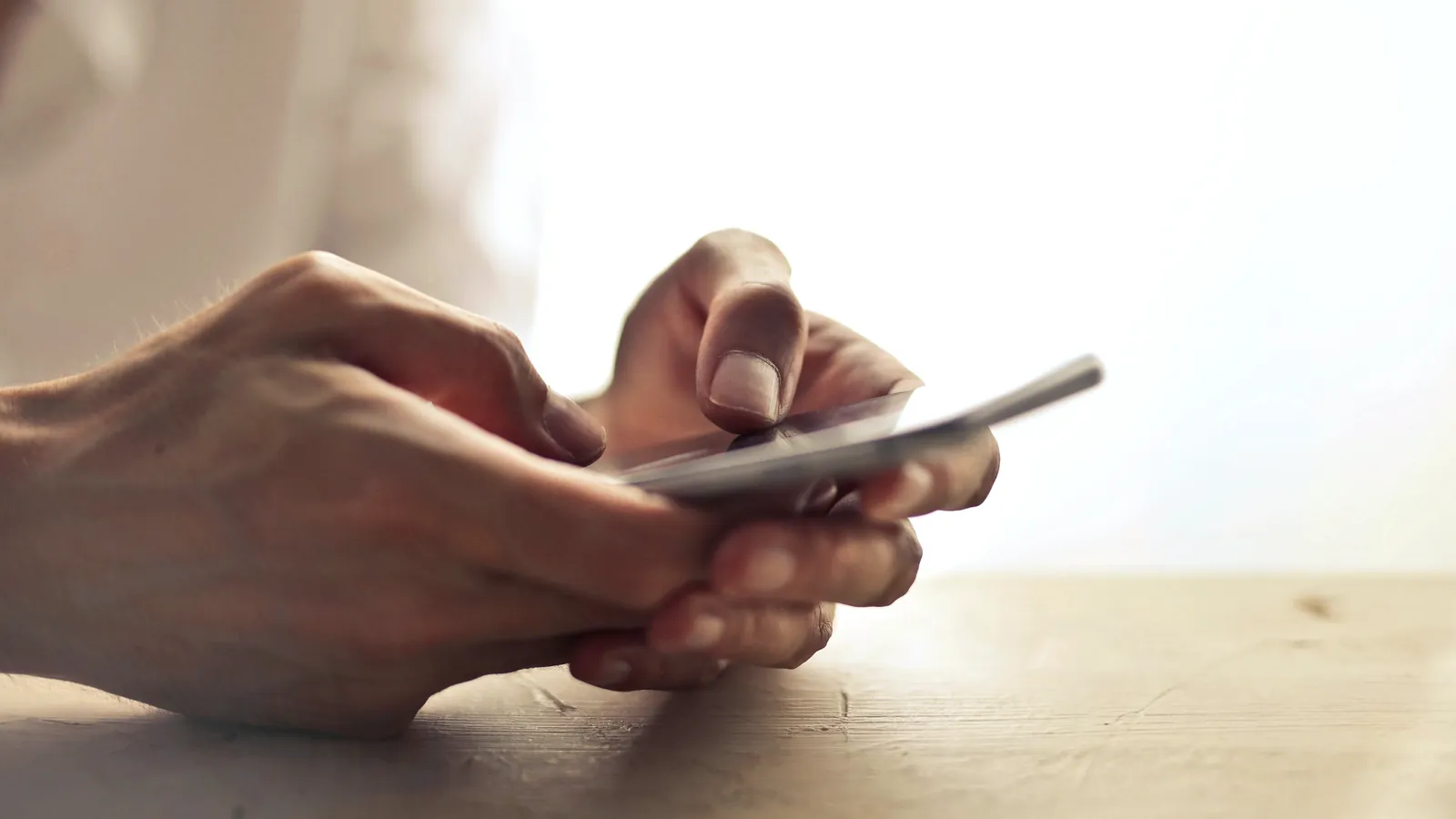 Manos que escriben un mensaje en el celular sobre una mesa