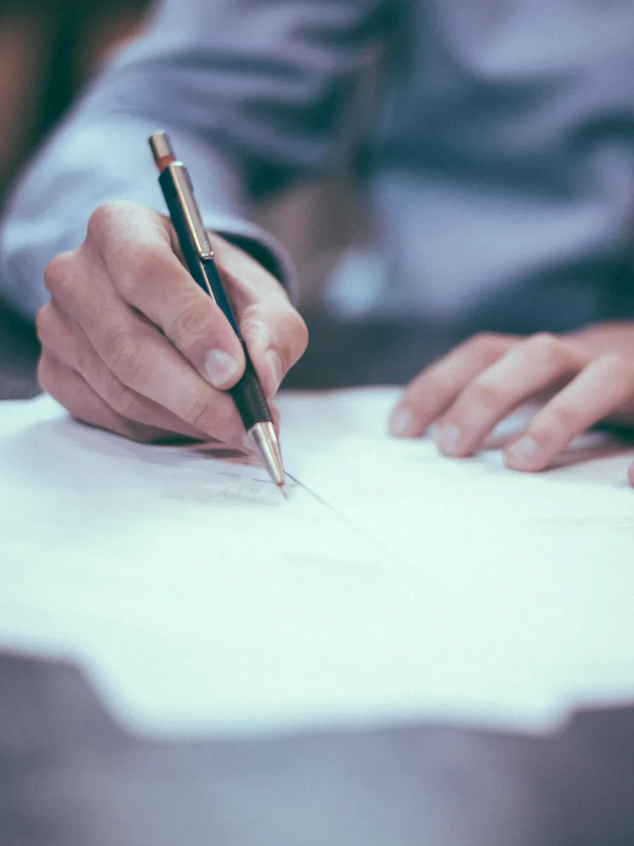 Manos de una persona firmando un documento sobre un escritorio