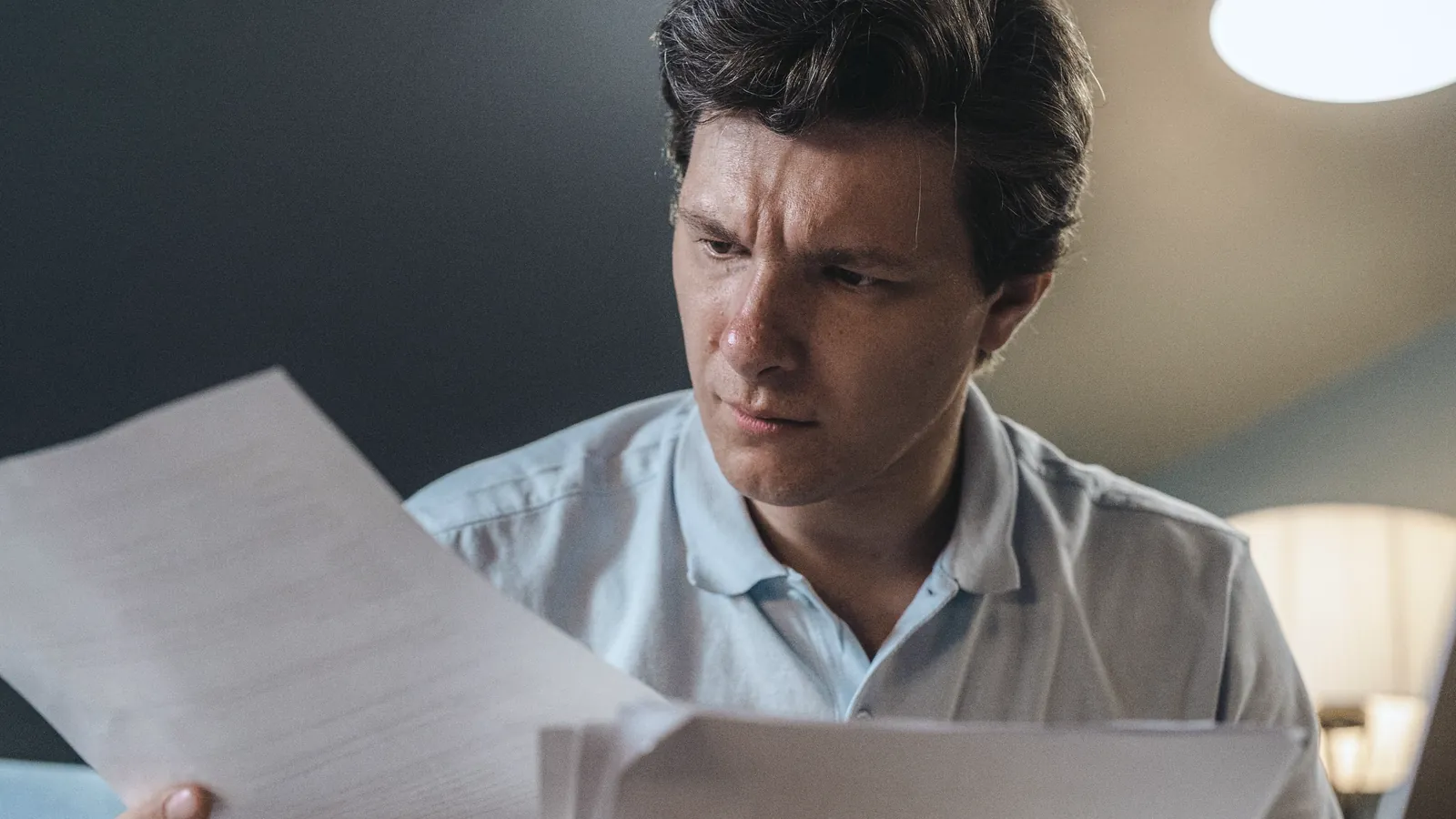 Hombre revisa con preocupación unos documentos impresos en su casa