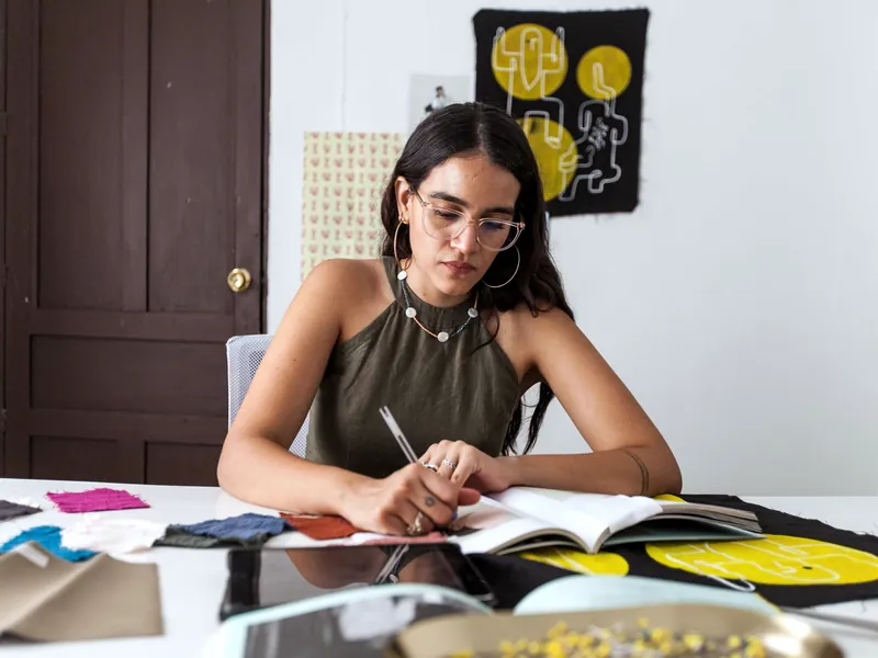 Diseñadora toma notas en su mesa de trabajo entre muestras de tela