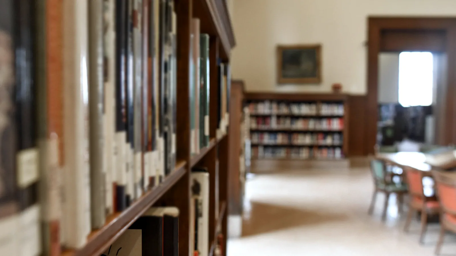Estantes de una biblioteca desenfocados y una sala de lectura luminosa al fondo